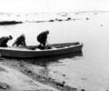 Three unidentified men launching a Poole canoe